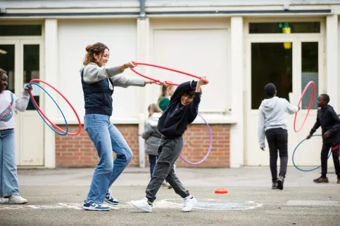 Un jeune en train de jouer dans la récréation avec un cerceau et une jeune femme. 