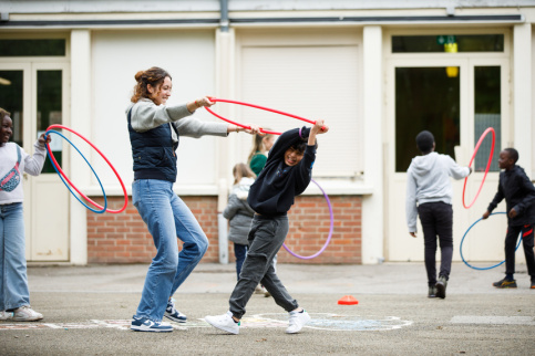 Un jeune en train de jouer dans la récréation avec un cerceau et une jeune femme.